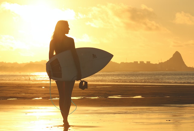 Woman carrying surfboards near seashore.
