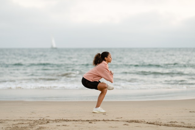 A woman in a pink sweater and black shorts doing yoga.